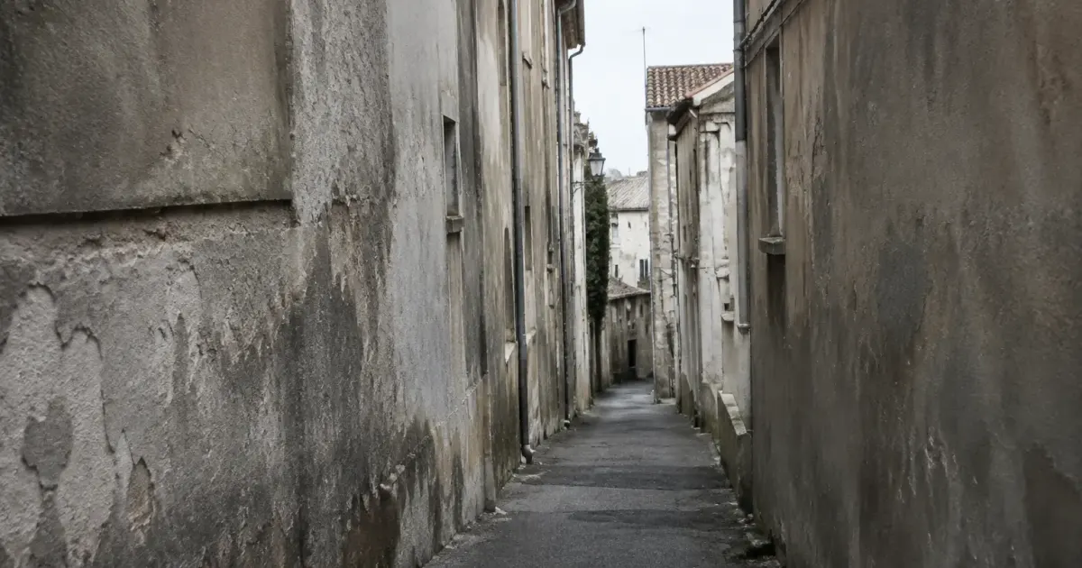 Murs gris delabres surplombant ruelle urbaine etroite et vide